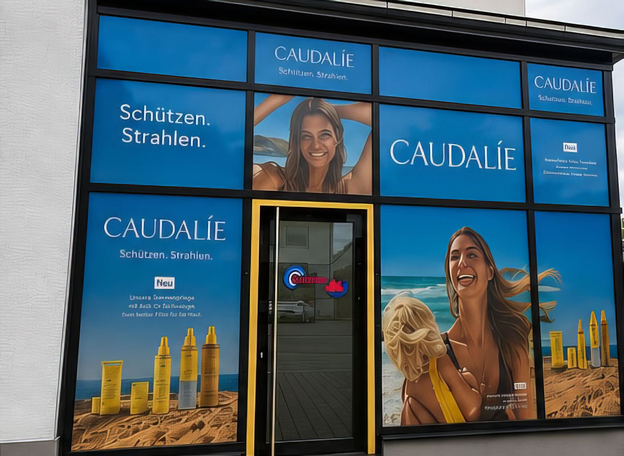 Geschäftsfront mit großflächigen Caudalie-Werbegrafiken, die Hautpflegeprodukte sowie zwei Personen in sommerlicher Strandkulisse zeigen.